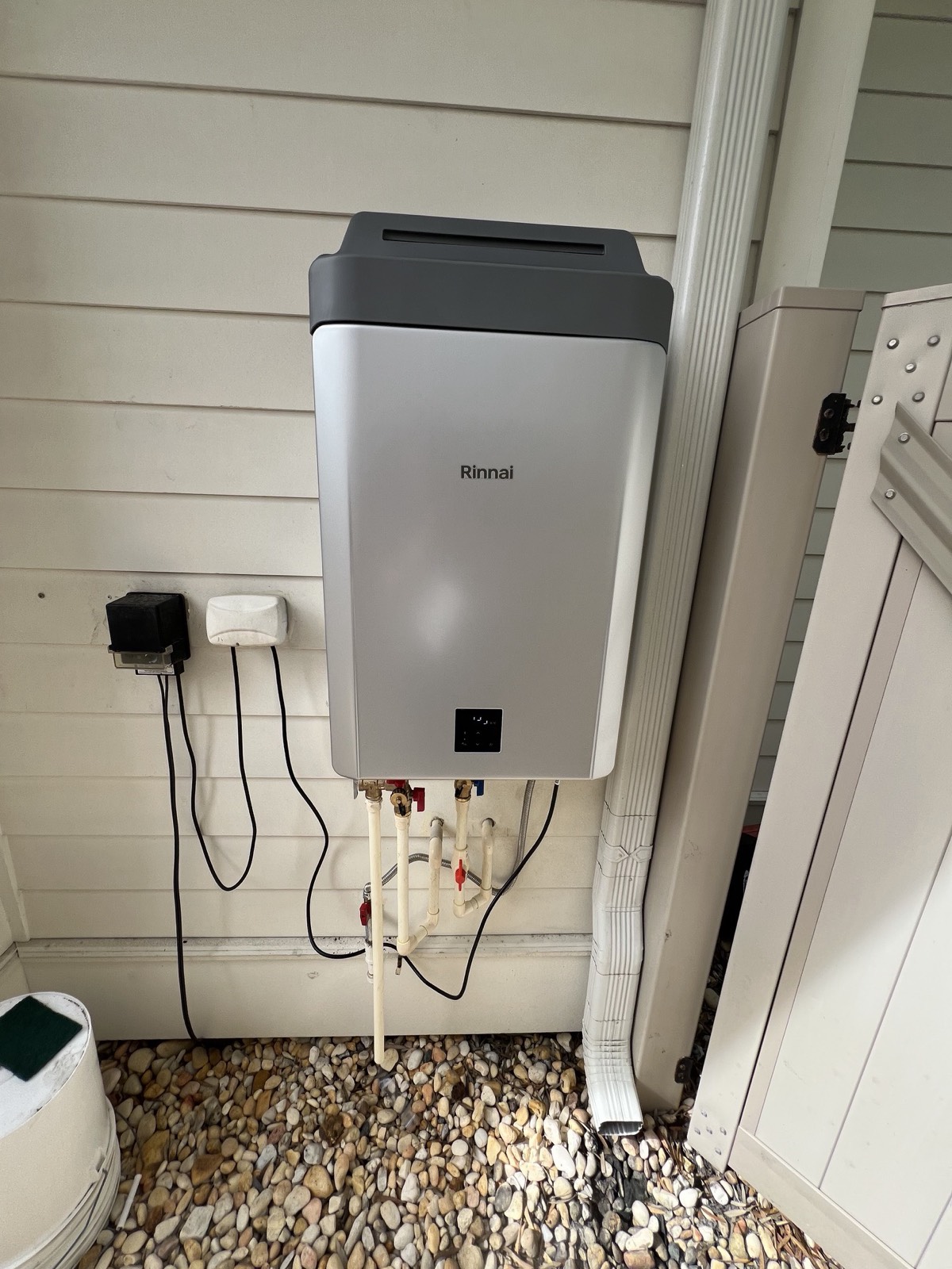 Rinnai tankless water heater installed outdoors with isolation valves above a gravel bed