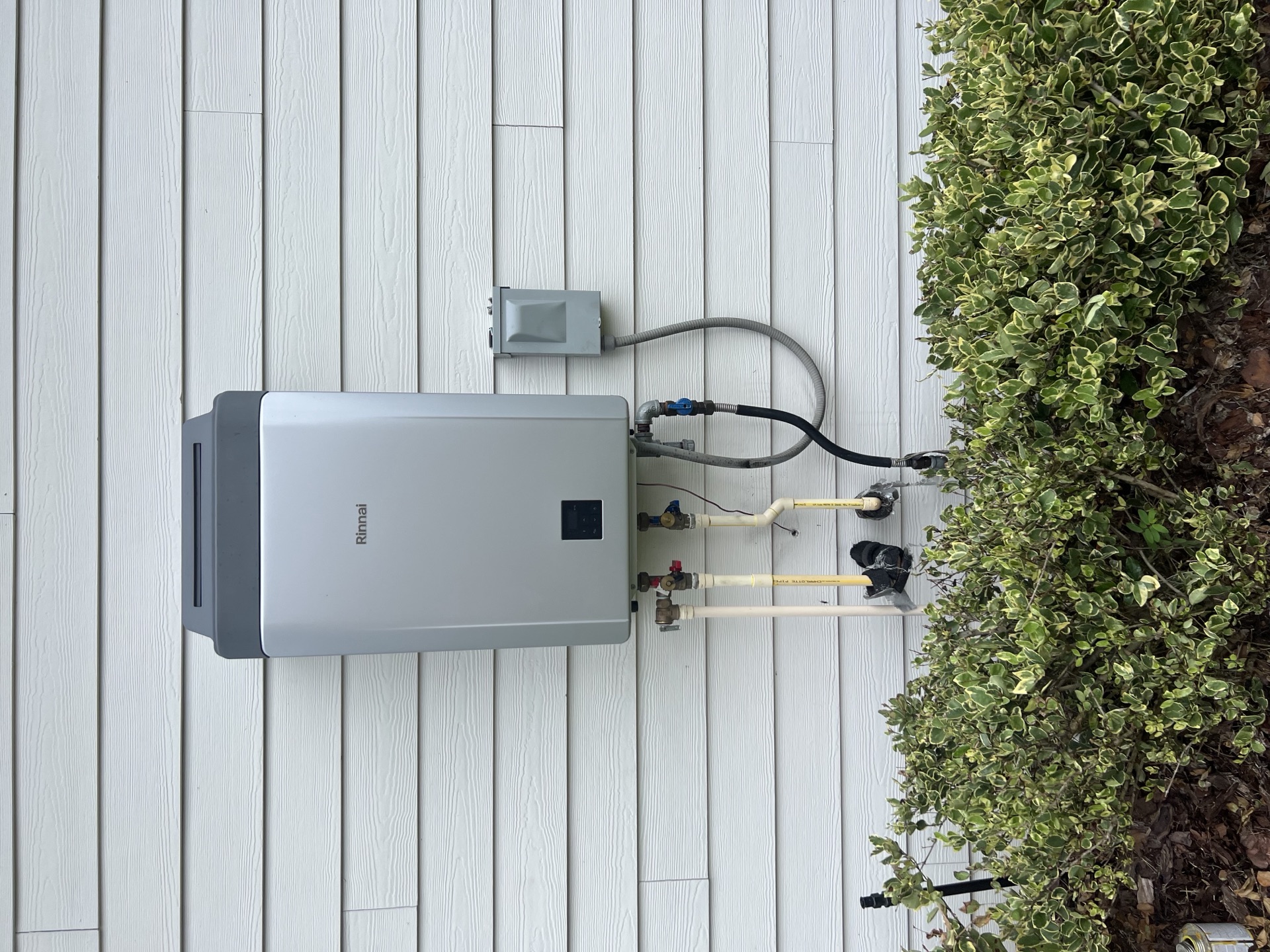 Close-up of a Rinnai tankless water heater installed on a Fernandina Beach home with copper supply lines and isolation valves